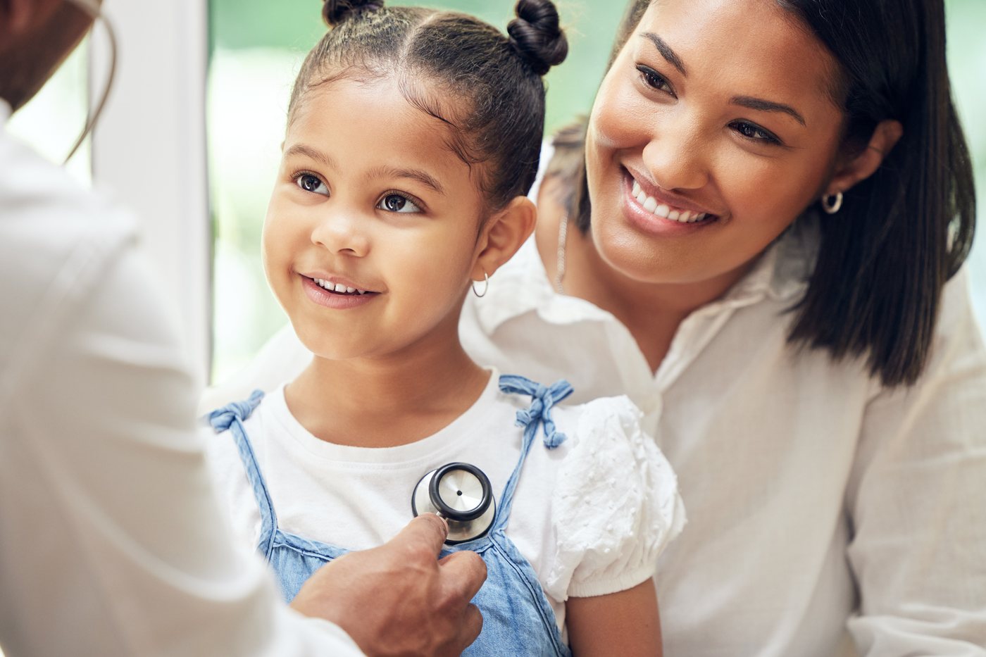 Children's health check: a doctor listening to a young girl's chest with a stethoscope beside her mother