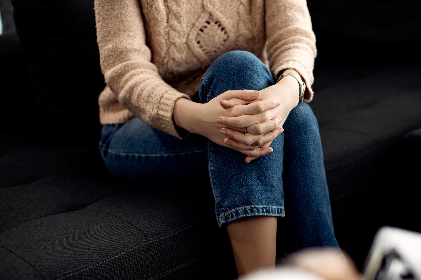 Mental health support: a person on a couch with hands clasped, talking with a health professional